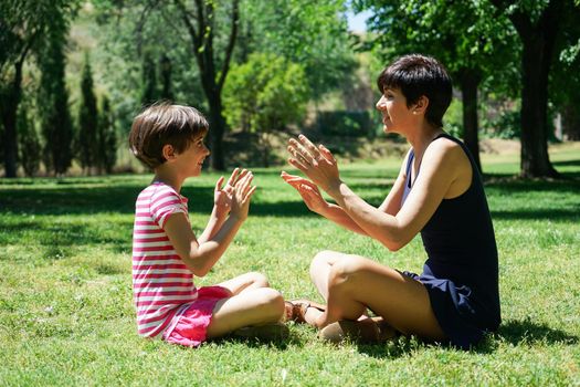 Mother and daughter playing with hands in city park. Happy loving family.
