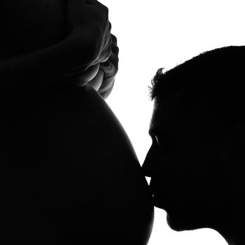 Man kissing his pregnant wife's belly in black and white
