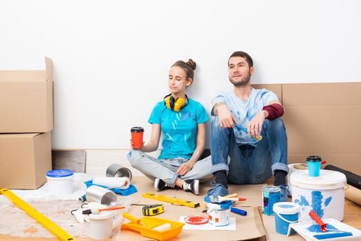 Happy couple together sitting on floor among cardboard boxes. Young man and woman relaxing after moving in their new house. House remodeling and interior renovation. Families moving concept.