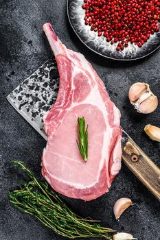 Raw tomahawk pork chop meat steak on a meat cleaver. Black background. Top view.