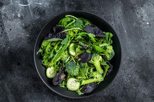 Fresh salad mix of spinach, arugula leaves, chard and lambs lettuce with vegetables. Black background. Top view.