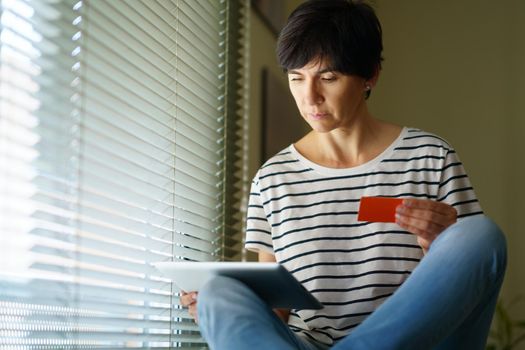 Middle-aged woman shopping online with her digital tablet paying with a credit card. Female in her 50s