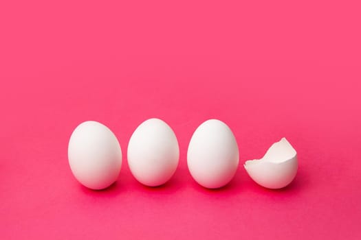 White chicken eggs placed in row near cracked eggshell against bright pink background