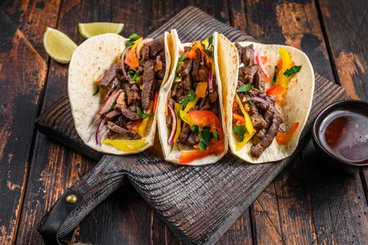 Tacos shells with pork meat, onion, tomato, sweet pepper and salsa. Mexican food. Dark wooden background. Top view.