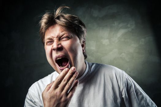 Young man yawning in studio over gray background