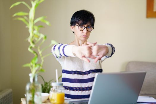 Woman teleworking from home with her laptop taking a stretch break.