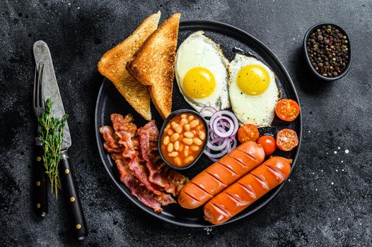 English breakfast with fried eggs, sausages, bacon, beans and toasts in a plate. Black background. top view.
