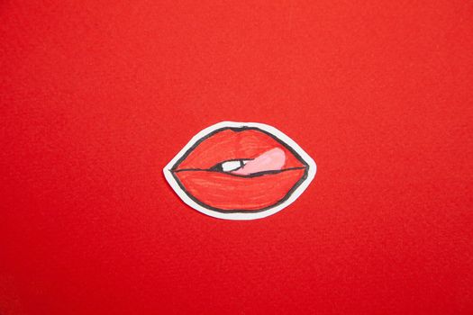 From above of painted sticker of tongue licking lips placed on red background