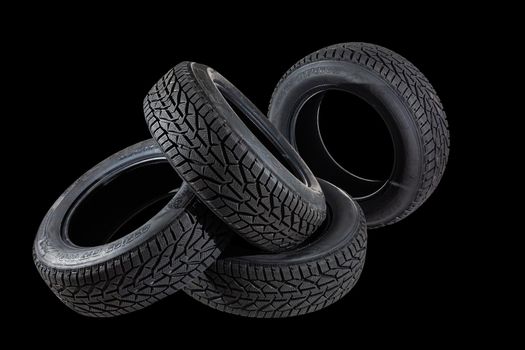 Stack of four new black tyres for winter car on black background