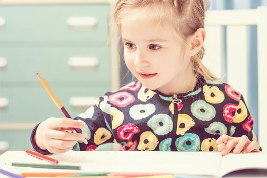 Charming blonde little girl with beauriful eyes draws with pencils and looks at camera