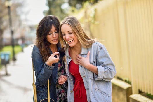 Two young women using the voice recognition of the phone. Girls sending a voice message with smart phone outdoors.