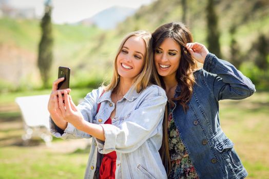 Two young women taking a selfie photograph in urban park. Lifestyle concept.