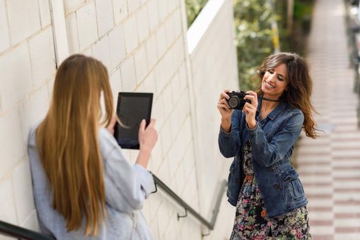 Two young tourist women taking photographs with digital tablet and analogic reflex camera. Travelers concept.