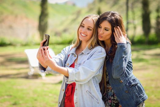 Two young women taking a selfie photograph in urban park. Lifestyle concept.