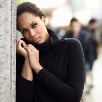 Young black female standing in an urban street. Mixed woman wearing poloneck sweater and skirt.