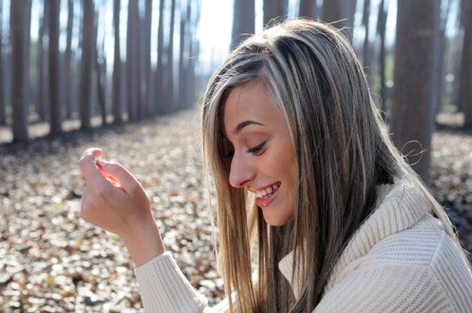 Beautiful blonde girl, dressed with a beige dress, standing in a poplar forest