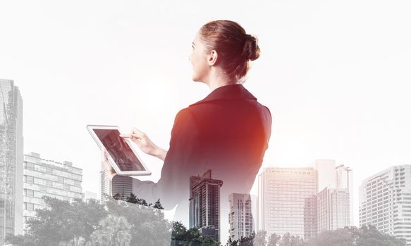 Young businesswoman using tablet computer. Double exposure concept with modern cityscape and beautiful woman in business suit. Digital technology in property management and development company.