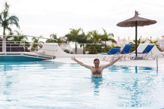 Young wet sexy muscular man posing in the swimming pool.