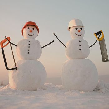 Snowman in winter outdoor. Building and repair work. Snowman builder in winter in helmet. Christmas or xmas decoration