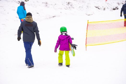 Instructors teach a child on a snow slope to snowboard