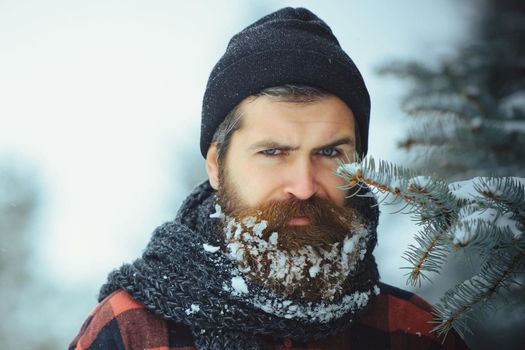 Christmas hipster. Winter portrait close up. Man with beard in winter forest with snow.