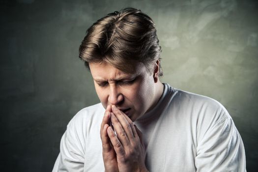 Young man praying on dark studio background