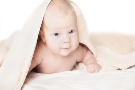 Cute baby under the towel after bathing lies smiling and looking in the camera on white background