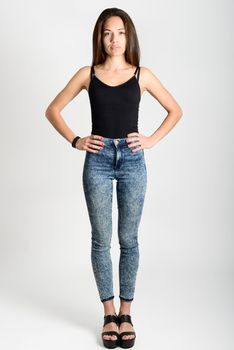 Young woman wearing black tank top and blue jeans on white background. Studio shot