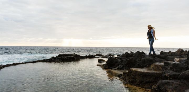 Women on volcanic rocks and blue ocean with waves, white foam and volcanic rocks. Canary Islands. The magnificent coast of the Atlantic Ocean.