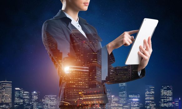 Businesswoman using tablet computer. Double exposure concept with night city and woman in business suit. Real estate investment. Digital technology in property management and development company.