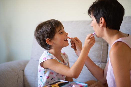 Happy beautiful mother and her little cute daughter doing make up for each other. Mum spending free time with her daughter.