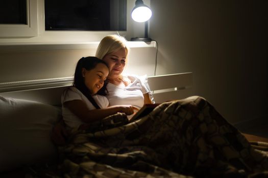 Family bedtime. Mom and child daughter reading a book in bed