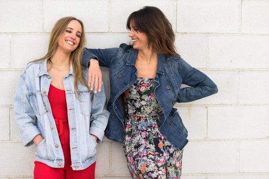 Two young women smiling in urban background. Happy girls on brick wall.