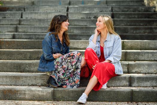 Two young women talking and laughing on urban steps. Two girls wearing casual clothes. Lifestyle concept.