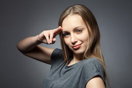 Smiling woman holding two fingers up to her eyebrow. Horizontal studio shot