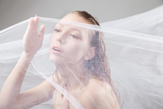 Close-up of beautiful wet woman face with waving fabric over light grey background