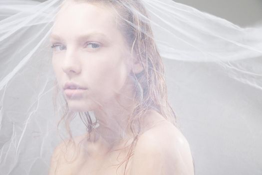 Close-up of beautiful wet woman face with waving fabric over light grey background