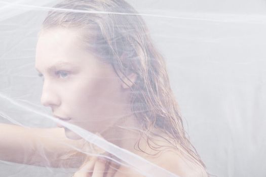 Close-up of beautiful wet woman face with waving fabric over light grey background