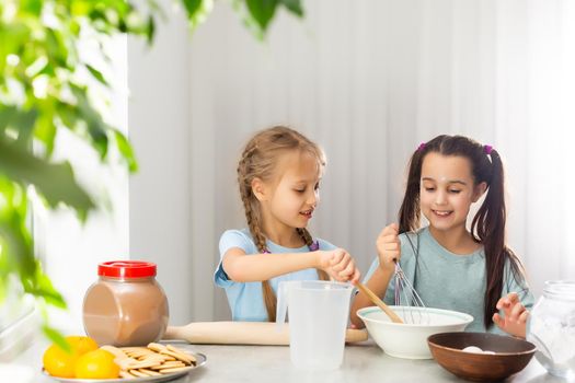 Two little girls in the kitchen prepare food, a dessert for the family. As they learn to cook they start playing with flour and smiling each other. Concept of: cooking classes, family, education.