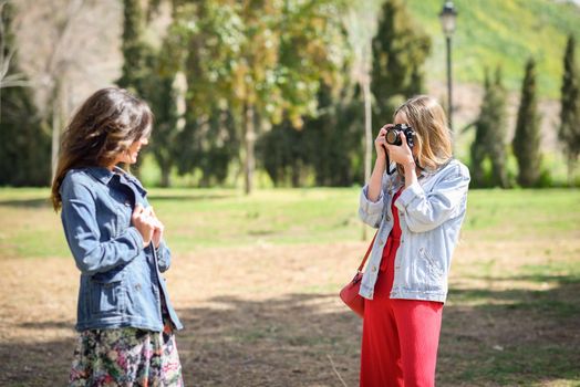 Two young tourist women taking photographs with analogic reflex camera in urban park. Travelers concept.