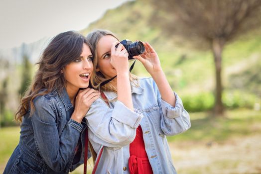 Two young tourist women taking photographs with analogic reflex camera in urban park. Travelers concept.