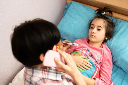 Mother worried about her daughter's temperature calling the doctor. Little girl on bed.