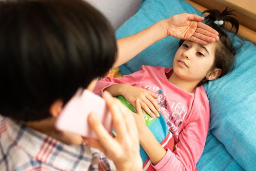 Mother worried about her daughter's temperature calling the doctor. Little girl on bed.