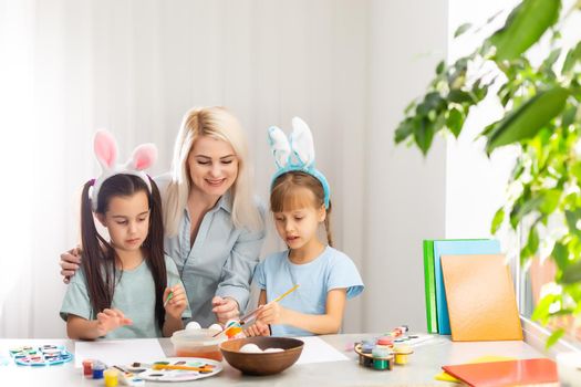Young mother and her two little daughters painting colorful Easter eggs at home