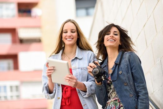 Two young tourist women looking maps with digital tablet outdoors. Travelers concept.