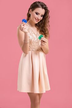 Beautiful young woman in dress with casino chips in the hands on pink background. Casino. Emotions. Gambling