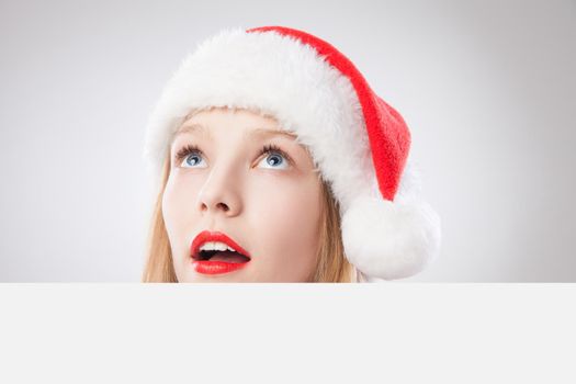 Beautiful christmas woman in santa hat holding empty board and looking to the left isolated on white background