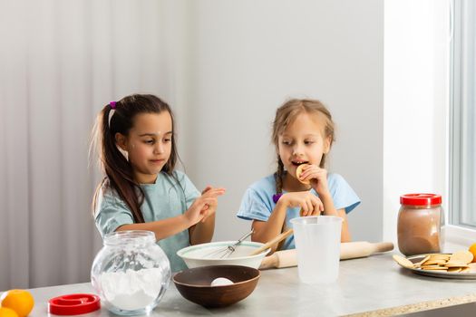 Two little girls in the kitchen prepare food, a dessert for the family. As they learn to cook they start playing with flour and smiling each other. Concept of: cooking classes, family, education.