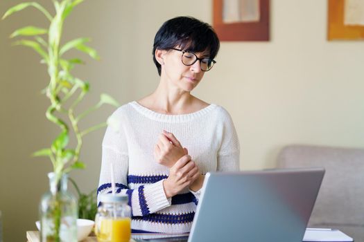 Woman teleworking from home with wrist pain having a massage to rest. Female using laptop.