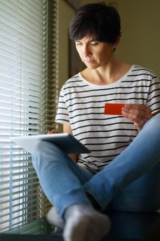 Middle-aged woman shopping online with her digital tablet paying with a credit card. Female in her 50s